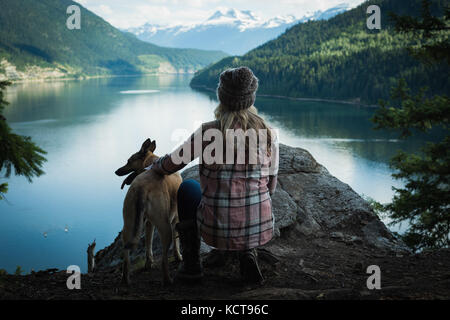 Vista posteriore della donna con cane rilassante vicino al fiume Foto Stock