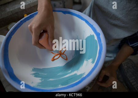 Maschio di vasai pittura a mano una ciotola nel laboratorio di ceramica Foto Stock