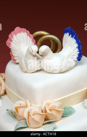 Primo piano della white iced torta di nozze con due colombe bianche e gli anelli di nozze una decorazione sulla parte superiore Foto Stock