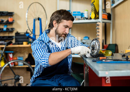 Giovane riparatore che fa il suo lavoro in un negozio di biciclette Foto Stock