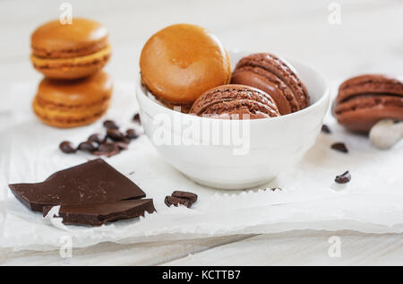 Pezzi di cioccolato sciolto con i chicchi di caffè e caffè aromatizzati macarons in una ciotola bianco presentato su un tovagliolo bianco Foto Stock