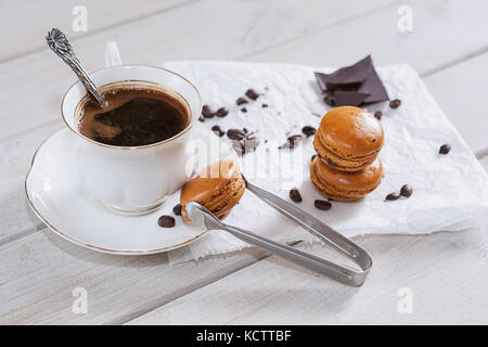 Pezzi di cioccolato con una tazza di caffè presentata su un tovagliolo bianco decorato con sciolto i chicchi di caffè e caffè aromatizzati macarons Foto Stock