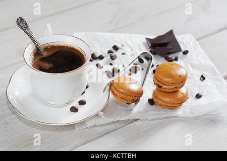 Pezzi di cioccolato con una tazza di caffè presentata su un tovagliolo bianco decorato con sciolto i chicchi di caffè e caffè aromatizzati macarons Foto Stock