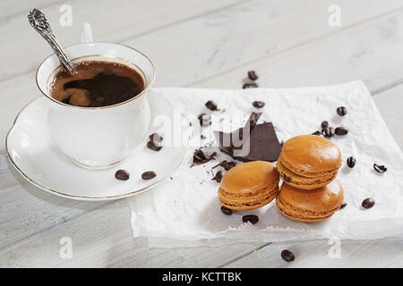 Pezzi di cioccolato con una tazza di caffè presentata su un tovagliolo bianco decorato con sciolto i chicchi di caffè e caffè aromatizzati macarons Foto Stock