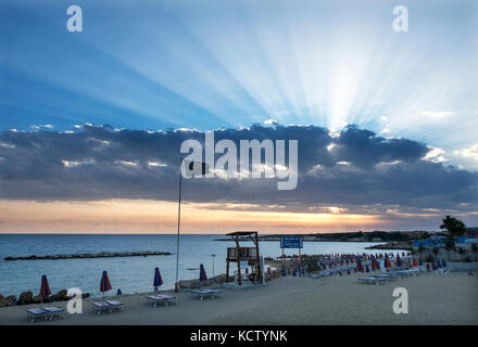 Sunray scoppiare attraverso da dietro le nuvole a Coral Bay in Peyia distretto, vicino a Paphos, Cipro. Foto Stock