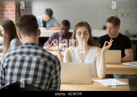 Calma imprenditrice meditazione yoga in posa in ufficio moderno impostazione. business lady prendersi cura della sua salute durante la pausa. ridurre il disagio al lavoro Foto Stock