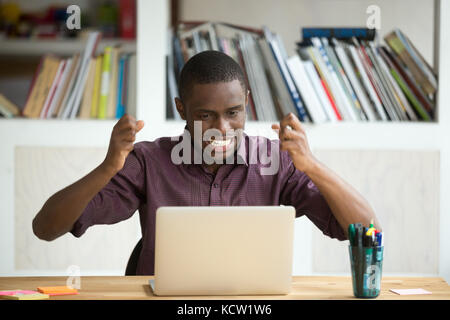 Dipendente emotivo frustrato che guarda lo schermo di un notebook. Il giovane imprenditore afroamericano si agitò vedendo le statistiche cadere, ricevendo l'applicazione Foto Stock