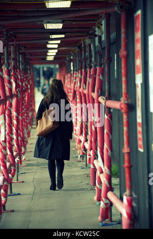 Ponteggio tunnel rossa ragazza distante figura maschile a piedi attraverso visto da dietro la scena cittadina street Foto Stock