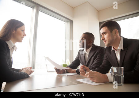 Multinazionale per i manager responsabili delle assunzioni conducendo intervista con caucasian giovane donna in abbigliamento formale. millenaria candidato donna rispondendo alle domande su meeti Foto Stock