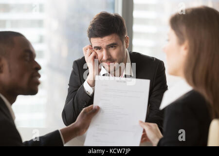 Preoccupato per il lavoro maschile candidato interessato in compagnia vacante ansiosamente cercando su multinazionale di reclutatori di analizzare e discutere il suo curriculum vitae sul intervie Foto Stock