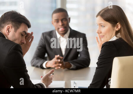 Scettico femmina e maschio caucasico i datori di lavoro che ricopre la faccia con la mano e sussurra mentre discutete african american candidato. deluso mana hr Foto Stock