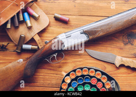 Attrezzature di caccia. Fucile da caccia, cartucce da caccia e caccia coltello su un tavolo di legno. Foto Stock