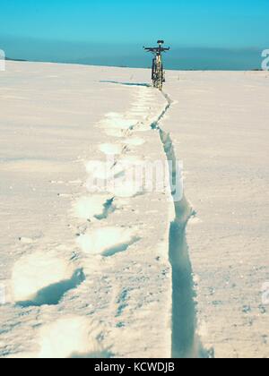 Mountain bike soggiorno in polvere di neve. perso il percorso nel cumulo di neve profonda. ruota posteriore dettaglio. fiocchi di neve di fusione su dark off road pneumatico. inverno meteo in Foto Stock