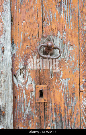 Dettaglio di un vecchio e addolorato porta in legno tavole, con weathered vernice marrone e un manico di bronzo con una toppa di chiave. Foto Stock