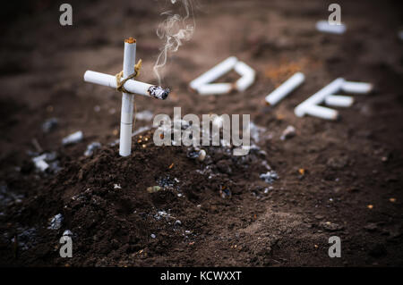 Una croce da butts. Il fumo uccide parola die cui le sigarette per terra accanto alla tomba. Il concetto di anti-fumo. Foto Stock