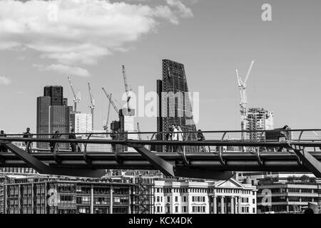 In bianco e nero di immagini in bianco e nero di persone a piedi attraverso la passerella del millennio attraverso il fiume Tamigi a Londra Regno Unito con lo skyline Foto Stock