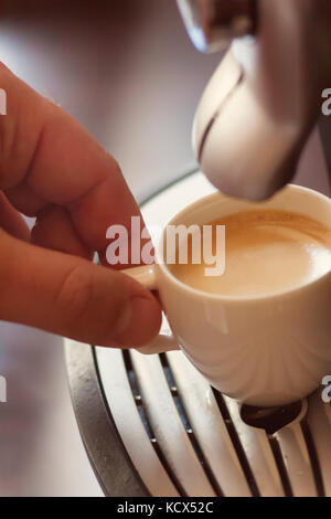 Vista ravvicinata della mano di un uomo che lavora in una casa di caffè la preparazione di caffè espresso in attesa per la macchina da caffè per terminare versando la beve fresco Foto Stock