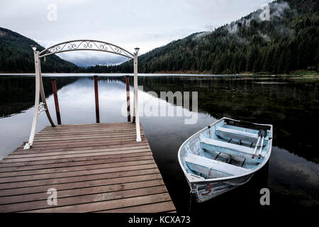 Un piccolo canotto è ancorata a un dock sul tranquillo lago specchio vicino sagle, Idaho. Foto Stock