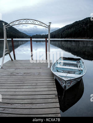 Un piccolo canotto è ancorata a un dock sul tranquillo lago specchio vicino sagle, Idaho. Foto Stock