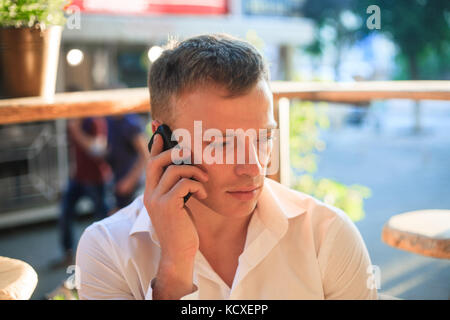 Ritratto di un giovane con un telefono in mani in un street cafe. Foto Stock