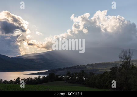 Bellissima vista del lago e delle colline, con raggi solari che filtrano attraverso le nubi e riflettendo su acqua Foto Stock