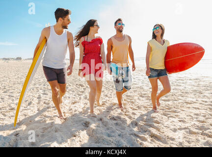 Amici camminare insieme in spiaggia e tenendo le tavole da surf Foto Stock