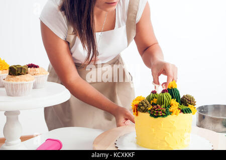 Un attraente giovane donna un pasticcere in una t-shirt bianco, un grembiule beige è adornata con una dieta giallo torta decorata con una verde crema di fagioli in una Foto Stock