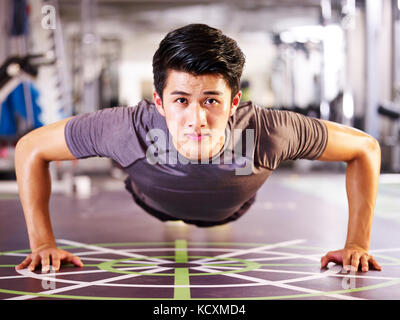Giovani asiatici uomo adulto esercizio in palestra facendo pushups, vista frontale. Foto Stock