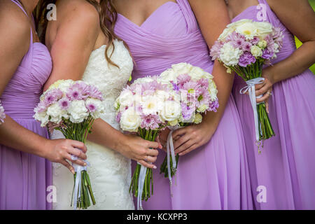 La sposa e le sue damigelle hanno tre indossando lilla o abiti di porpora tenendo una bella disposizione di lavanda e mazzi di fiori bianchi. Foto Stock