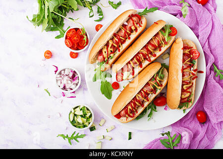 Hot Dog con salsiccia pancetta, cetriolo, pomodoro e cipolla rossa sulla piastra bianca. vista dall'alto. flat laici. Foto Stock