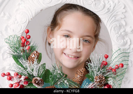 Bella sorridente bambina sullo sfondo delle decorazioni natalizie da abete coni e filiali Foto Stock