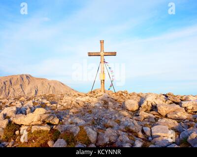 Grande croce sulla cima della montagna come tipico delle Alpi. croce di legno al picco di montagna con la preghiera buddista flags flutter in forte vento. Monumento a vi Foto Stock