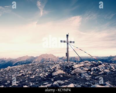 Grande croce sulla cima della montagna come tipico delle Alpi. croce di legno al picco di montagna con la preghiera buddista flags flutter in forte vento. Monumento a vi Foto Stock