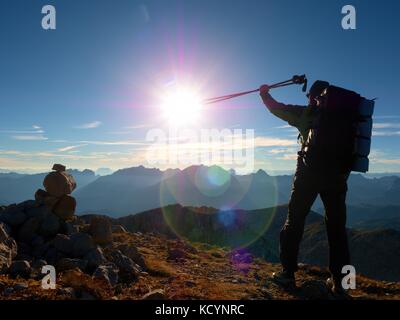 Lens Flare leggero, forte difetto. tall backpacker con pali in mano. tempo soleggiato nelle montagne rocciose. escursionista con zaino grande stand sul roccioso poi vista Foto Stock