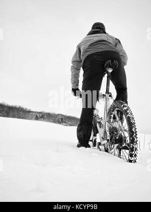 Sportivo con mountain bike perso nella neve. perso il percorso nel cumulo di neve profonda. fiocchi di neve di fusione su dark off road pneumatico. inverno meteo nel campo. Foto Stock