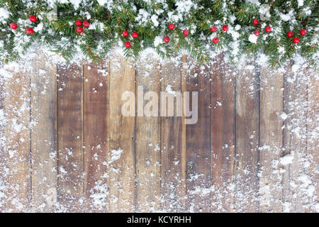 Natale fuori confine naturale del albero di natale Abete rami e bacche rosse su un marrone di sfondo di legno ricoperta di neve con copia spazio. Foto Stock