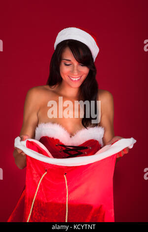 Giovane donna felice guarda in un sacchetto di santa su sfondo rosso Foto Stock