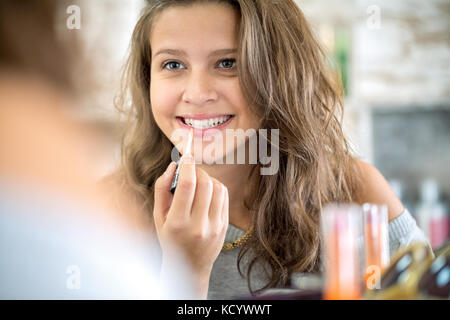 Carina ragazza adolescente applicando lip gloss, compongono specchio anteriore Foto Stock