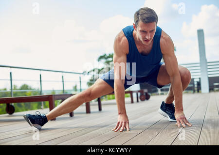 A piena lunghezza Ritratto di concentrato di giovani runner stretching gambe all'aperto durante la preparazione per la maratona, bel cielo blu su sfondo Foto Stock