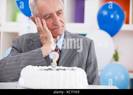 L'uomo anziano triste ha dimenticato quanto vecchio sta guardando la torta di compleanno con un punto interrogativo Foto Stock