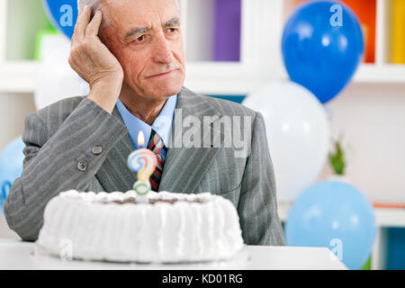 Uomo anziano seduto davanti alla torta di compleanno e cercando di ricordare quanto è vecchio Foto Stock