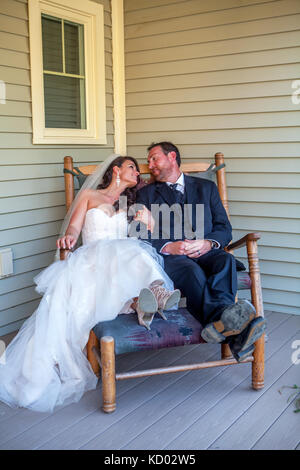 Sposi seduto in una sedia a dondolo che indossano i loro smoking e abito da sposa. Foto Stock