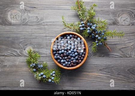 Ciotola di legno con semi di ginepro. Filiale di Juniper con bacche. Bacche di ginepro in una ciotola con uno sprig. Foto Stock