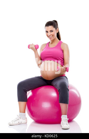 Donna incinta facendo bicipite muscolare utilizzando manubri seduto su una sfera di fitness Foto Stock