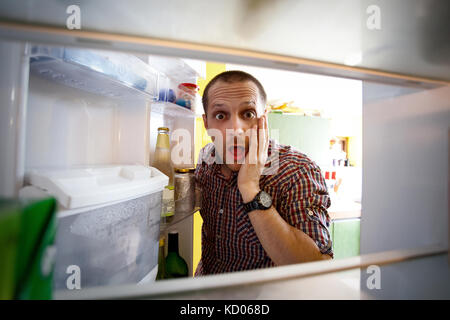 Scioccato gli uomini alla ricerca nel suo frigo vuoto Foto Stock