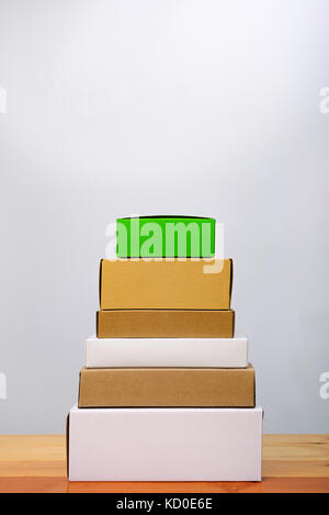 Gruppo della scatola di cartone di differente colore e dimensioni, pila del pacchetto costituito da carta per mock-up luminoso su un tavolo di legno con copia spazio. Foto Stock