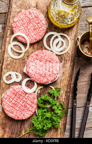 Carne cruda hamburger con cipolla e spezie in legno rustico sfondo, vista dall'alto Foto Stock