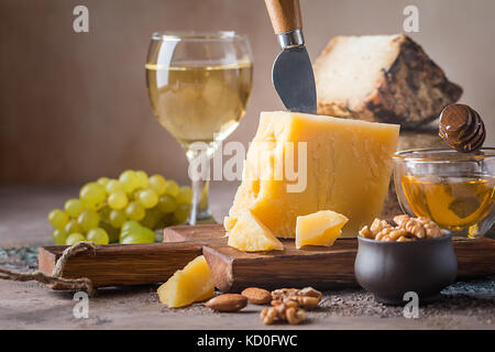 Vari tipi di formaggio con miele, uva e vino su sfondo rustico Foto Stock