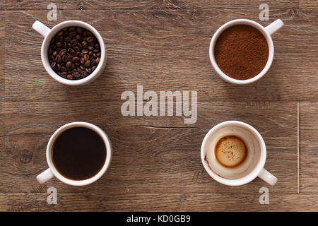 Varietà di tazze di caffè e caffè in grani sul vecchio tavolo in legno. quattro tazze di caffè, fasi di bere - fagiolo, terra e tazza vuota Foto Stock