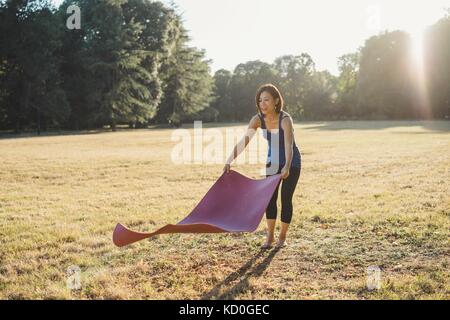 Donna matura nel parco, la posa di materassino yoga sull'erba Foto Stock